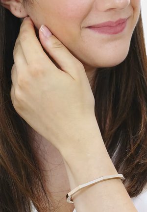 Bracciale in oro rosa con forma rettangolare; presenta un design a linee orizzontali testurizzate; indossato su un polso, mano vicino al viso.