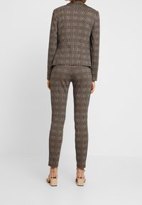 Costume à carreaux marron avec veste sur mesure et pantalon ajusté. Présente un tissu texturé avec un mélange de motifs foncés et clairs.