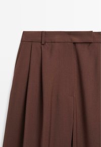 Braune weit geschnittene Hose mit geradem Beinausschnitt, breitem Bund und glatter Textur. Keine sichtbaren Beschläge oder Muster.