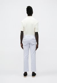 Valkoinen teksturoitu lyhythihainen paita ja vaaleanharmaat housut, nähtynä takaa, mustat slip-on-kengät, joissa juttikoriste.