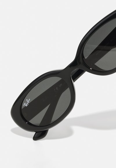Lunettes de soleil noires avec des verres ovales et une monture en plastique brillante. Les verres sont sombres et le nom de la marque est visible sur un des verres.