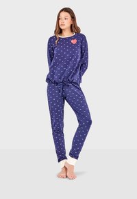 Ensemble de pyjama bleu marine avec des motifs de cœurs blancs, comprenant un haut à col ras du cou avec un patch en forme de cœur et un pantalon à taille élastique avec des poignets.