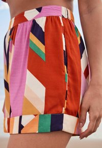 Barevné šortky s vzory obsahují geometrické tvary v odstínech červené, růžové, zelené, oranžové a námořnické modři. Vyrobené z lehkého materiálu s volným střihem.
