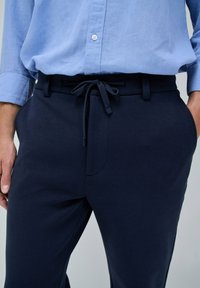 Pantalones azul marino fabricados en tejido suave, con una cinturilla elástica y cordón ajustable, bolsillos laterales y una textura lisa.