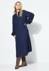 Navyblauwe, lange mouwen, knopen-overhemdjurk met een gelaagde rok en zijzakken, gecombineerd met bruine cowboylaarzen. Gelaagd stof.