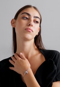 Pulseira de prata com um design de corrente torcida e um pingente, usada numa mão contra um fundo neutro, apresentando uma textura suave e polida.