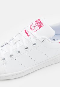 Vita lädersneaker med rosa logotyp på tungan, perforerade detaljer på sidorna och vita snörningar. Gummisula med bra grepp.