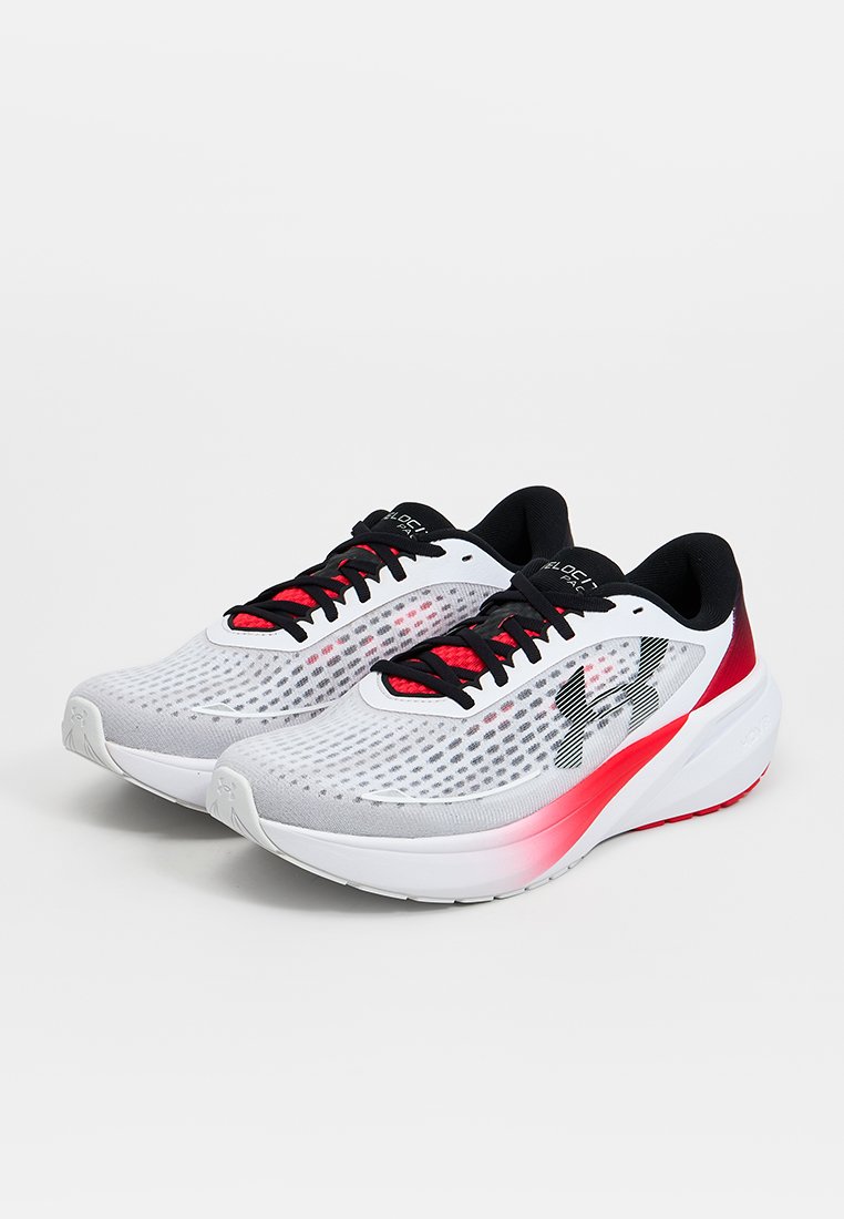 Par de zapatillas de correr blancas y rojas con cordones y logotipos negros, parte superior de malla y suelas acolchadas gruesas sobre un fondo liso.