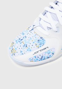 Baltas sporta apavi ar ziedu rakstu zilā un dzeltenā krāsā. Iekļauti sieta paneļi un "Jordan" logo. Gluda tekstūra un izliekta forma.
