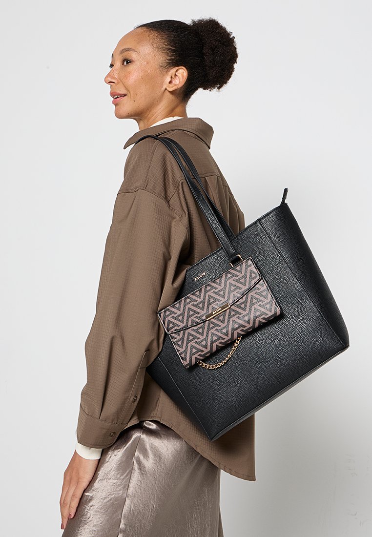 Bolso tote de cuero negro con un bolsillo adjunto de patrón geométrico en tonos rosa y marrón. El bolsillo cuenta con un acento de cadena dorada y cierre magnético.
