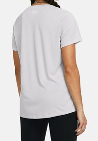 Camiseta gris de manga corta con un ajuste holgado, hecha de tejido suave. Presenta un pequeño logo en la parte superior de la espalda. Textura suave.