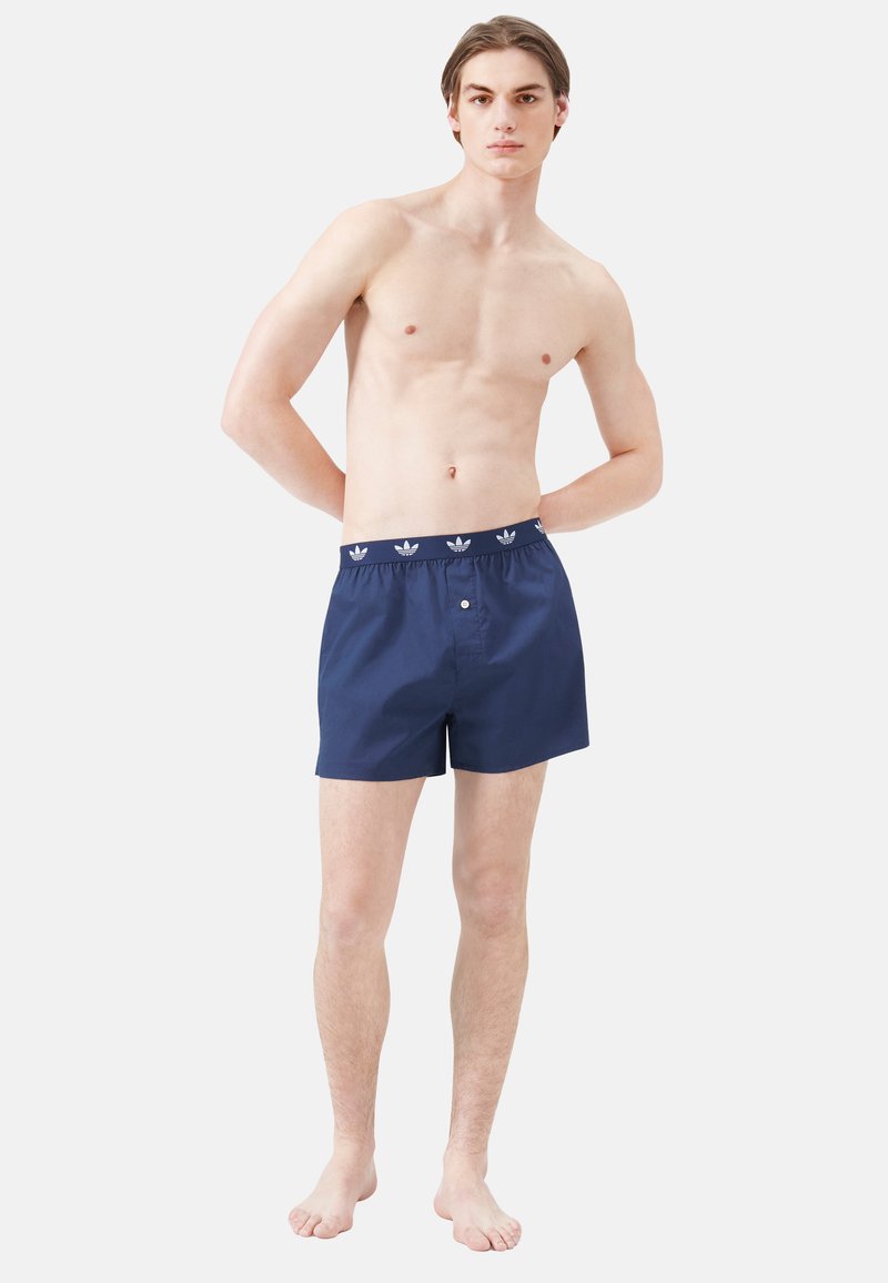 Pantaloni da bagno blu navy con vita elastica, caratterizzati da un motivo a logo bianco, realizzati in tessuto leggero, con un dettaglio a pulsante sulla parte anteriore.