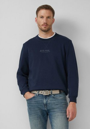 Dunkelblaues Sweatshirt mit Rundhalsausschnitt und langen Ärmeln, mit einem kleinen S.Oliver-Logo in der Mitte. Getragen über hellblauen Jeans und einem grauen Gürtel.