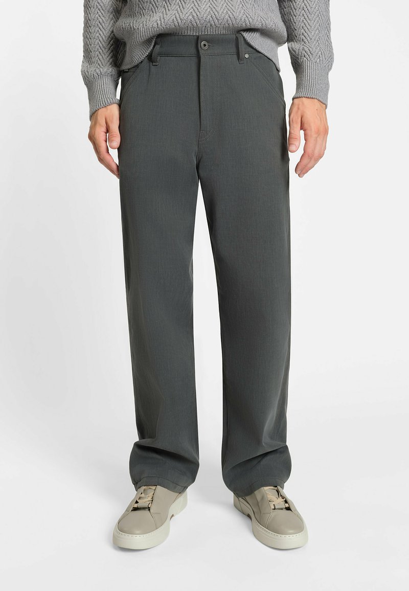 Dunkelgraue, weit geschnittene Hosen mit glatter Textur, Gürtelschlaufen, Knopfverschluss und subtilen Steppdetails, kombiniert mit hellen Sneakers.