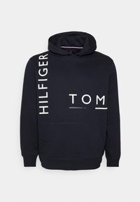 Dark navy hooded sweatshirt made of cotton blend, featuring large white text "TOM HILFIGER" on the front and a kangaroo pocket.