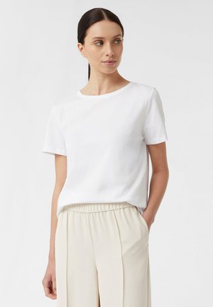Witte T-shirt met korte mouwen en een ronde hals, gemaakt van zachte stof. Gepaard met lichtbeige, loszittende broek met zijzakken.