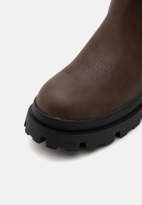 Bottette en cuir marron avec une finition texturée, dotée d'une semelle épaisse en caoutchouc noir avec un motif à crampons et un bout arrondi.