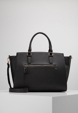 Sac cabas en cuir noir texturé avec double poignée, poche zippée avant et bandoulière amovible, présenté sur un piedestal blanc.
