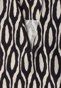 Tissu noir et blanc avec un motif ovale géométrique et un col en V montrant une couche intérieure partielle.