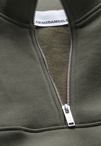 Olivgrüner Reißverschluss-Sweatshirt mit silbernem Reißverschluss und weicher innerer Auskleidung. Markenlabel im Kragen sichtbar.
