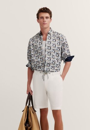 Short-sleeve shirt with blue and floral pattern, paired with white shorts. Holds a tan handbag with dark brown accents.