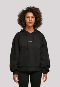 Black oversized hoodie made of soft fabric, featuring a front logo detail, adjustable drawstring hood, and ribbed cuffs.