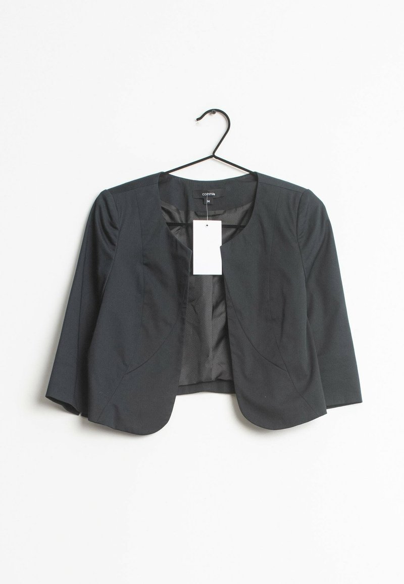 Blazer noir court pour femme avec manches trois-quarts, devant ouvert et une étiquette rectangulaire blanche suspendue au col sur un cintre noir.