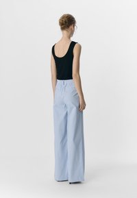 Top aderente nero e pantaloni larghi a righe verticali blu chiaro con vita elastica. Tessuto liscio e silhouette rilassata.