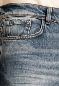 Light blue denim jeans with a faded wash, featuring orange stitching and a small pocket detail, close-up view of the waistband and pocket.