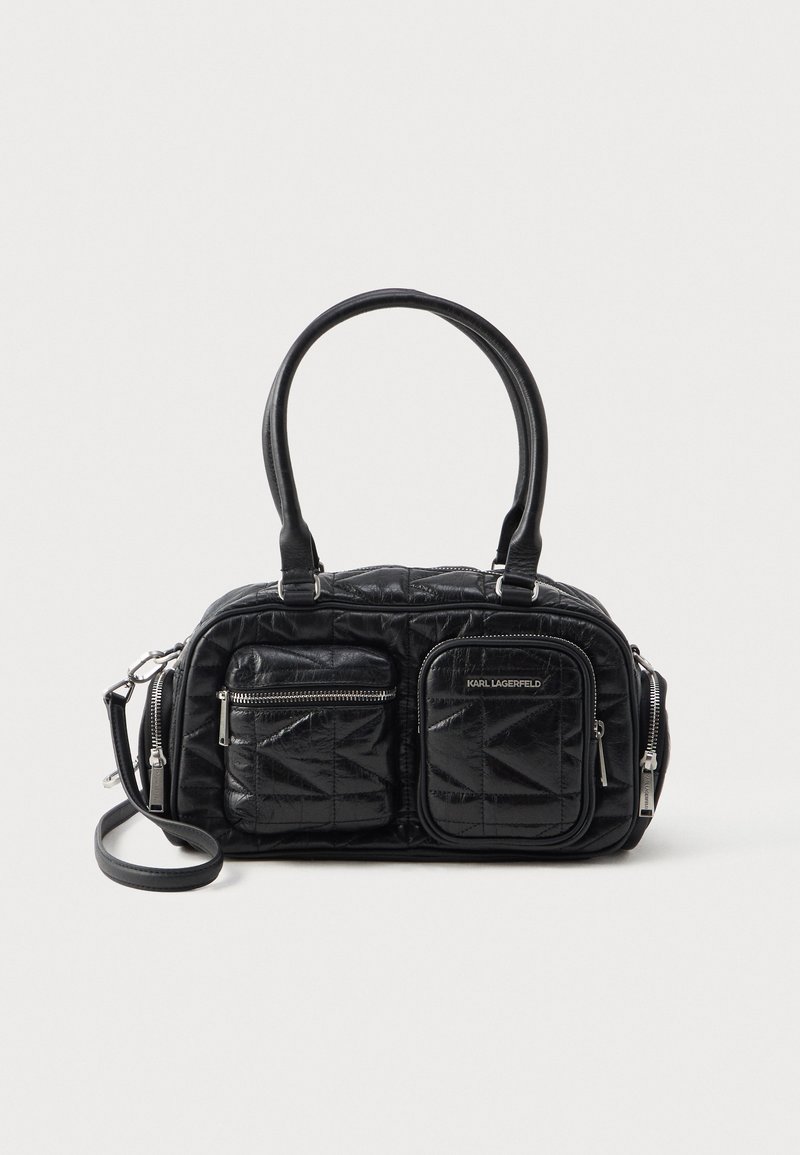 Černá prošívaná kabelka vyrobená z umělého materiálu, s dvěma předními zipovými kapsami a odnímatelným ramenním popruhem. Hladký povrch, zaoblený tvar.