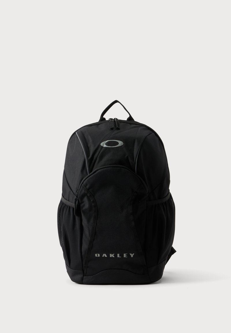 Μαύρο σακίδιο Oakley με μπροστινή τσέπη με φερμουάρ, πλαϊνές δίχτυνες τσέπες, επάνω χερούλι και λογότυπο στο μπροστινό μέρος σε απλό φωτεινό φόντο.