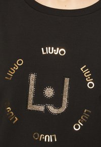 Czarny bawełniany T-shirt z centralnym wzorem "LJ" w metalicznym złocie i cyrkoniach, z tekstem "LIUJO" ułożonym wokół.