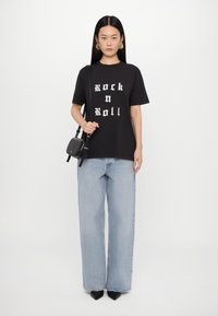 Svart bomullströja med vit "Rock n Roll" tryck, kombinerad med ljusblå vida jeans och svarta spetsiga klackar. Liten svart crossbody-väska.