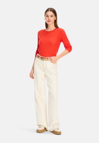 Rotes geripptes Langarmoberteil kombiniert mit cremefarbenen weiten Hosen und einem braunen Gürtel. Es hat einen runden Ausschnitt und einen lässigen Schnitt.