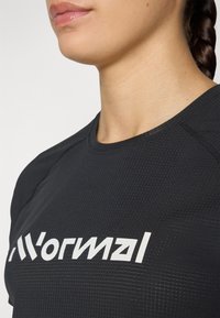 Svart teksturert treningsskjorte med rund hals og en fremtredende hvit logo. Stoffet ser lett og pustende ut.