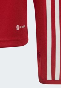 T-shirt de sport rouge fabriqué en tissu texturé, avec des rayures blanches sur les côtés et un logo "AEROREADY" près de l'ourlet.