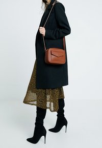 Borsa a tracolla in pelle marrone con finitura testurizzata, forma rettangolare e chiusura a patta. Presenta una lunga tracolla regolabile.