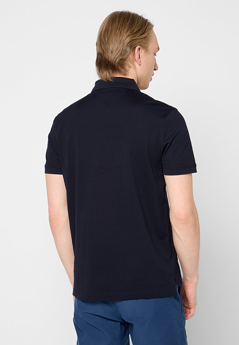 Polo shirt bleu marine à manches courtes, avec un col et des fentes sur les côtés de l'ourlet. Fabriqué dans un tissu lisse et respirant. Vue de dos présentée.