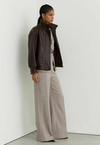 Pruun nahast jakk kõrge kraega, millel on tekstureeritud detailid. Sobitatud laia säärega, heledates toonides, mustriliste pükstega.