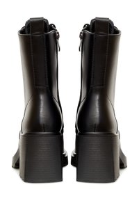 Bottines en cuir noir avec un talon épais et cranté, fermeture éclair et coutures renforcées. Texture lisse avec un design épuré.