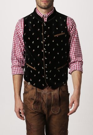 Homme portant une tenue traditionnelle bavaroise avec une chemise à carreaux rouges, un gilet noir brodé et un pantalon en cuir marron lederhosen.