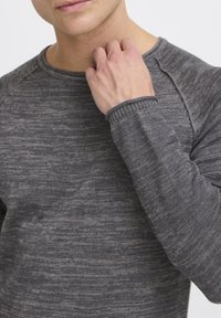 Grauer, strukturierten Langarmpullover mit Rundhalsausschnitt, der ein dezentes Muster und gerippte Bündchen aufweist, getragen von einer Person.