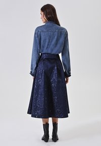 Jeanshemd met lange mouwen, gecombineerd met een hoogwaardig, donkerblauwe satijnen rok met een reliëf bloemenpatroon. Zwarte laarzen maken de outfit compleet.