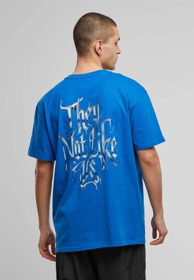 Blå bomulds T-shirt med et stort sølvdryppende grafisk tekst på ryggen, som læser "De kan ikke lide os." Korte ærmer og afslappet pasform.
