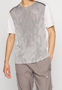 Herre atletisk t-shirt i gradient gråtoner. Mesh tekstur, korte ærmer, rund hals, med sorte accenter og subtile brandingdetaljer.