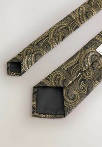 Čierny motýlik s pozláteným paisley vzorom, s hladkou hodvábnou textúrou a šikmými koncami. Jeden koniec má čiernu podšívku s etiketou.