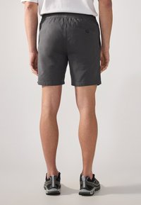 Pantalones cortos grises con una cinturilla elástica y un único bolsillo trasero. El material parece ligero, con una textura suave y un acabado limpio.