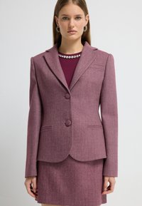 Lilla blazer med fiskebensmønster, to knapper, klapkrave og sidelommer, sat sammen med en matchende nederdel.