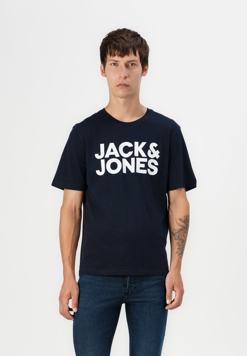Tamsiai mėlyna medvilninė marškinėlių su trumpomis rankovėmis, su dideliu baltu "JACK & JONES" logotipu priekyje. Klasikinio apvalaus kaklo dizainas.