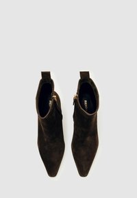 Brūni zamšādas potītes ar smailu purngali, rāvējslēdzēja detalizāciju un cilpu aizmugurē vieglai uzvilkšanai. Gluda tekstūra ar elegantu dizainu.